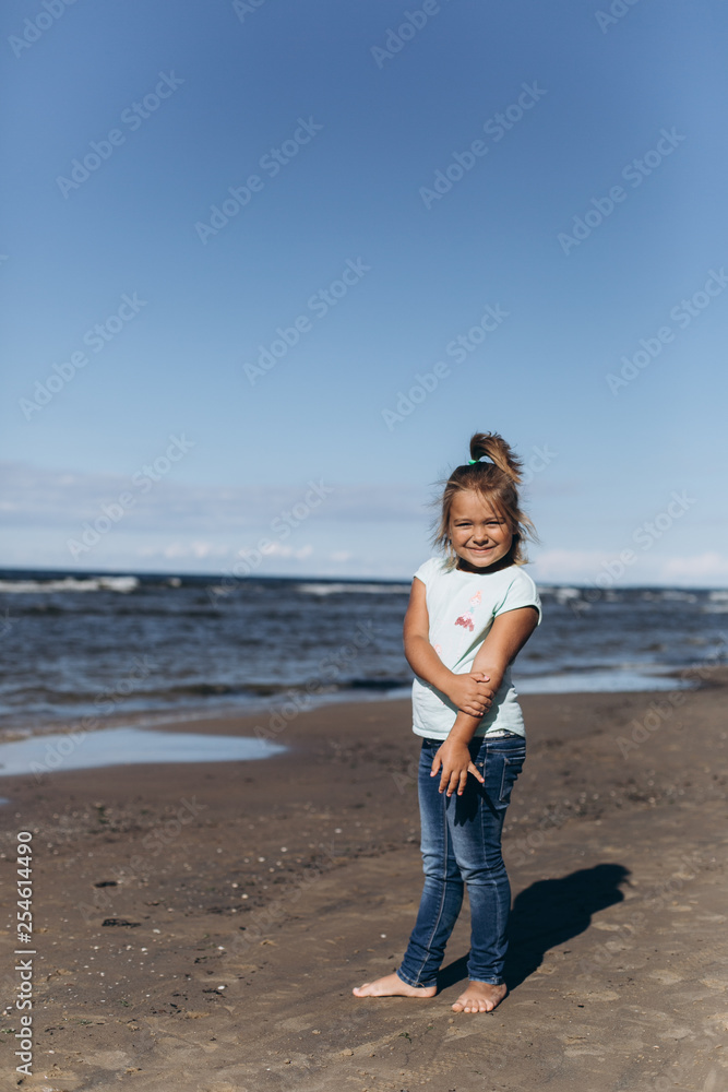 Cheerful happy girl running on the coast of the ocean with wind and waves. Happiness, activity, ocean, childhood concept