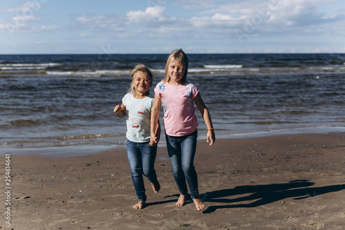 Cheerful happy girls running on the coast of the ocean with wind and waves. Happiness, activity, ocean, childhood concept