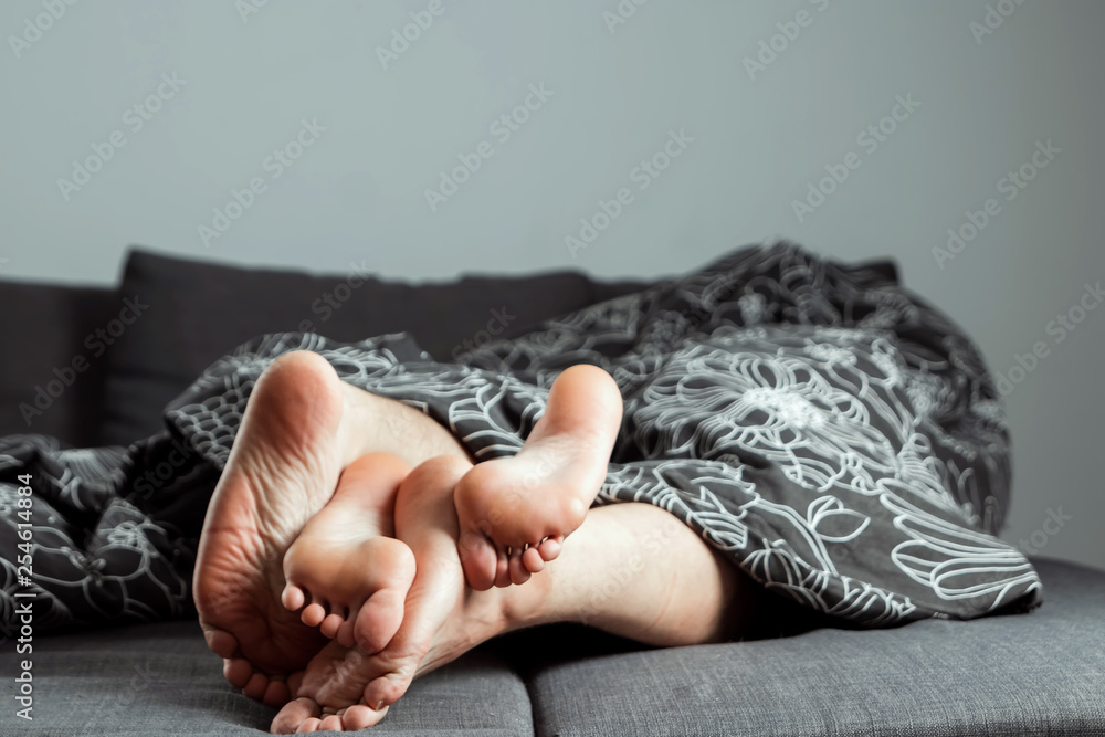 The legs, feet of a couple in love are sticking out from under the blanket.  Valentine's Day or love story. Prelude in bed, sex, adult sites, love,  relationships. Photos | Adobe Stock
