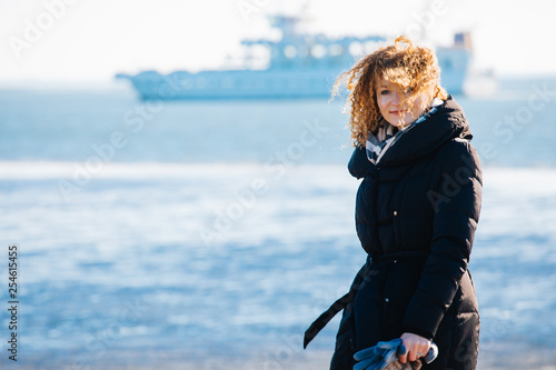 Curly girl on the background of the sea and the ship. Good mood, weekend, smile.