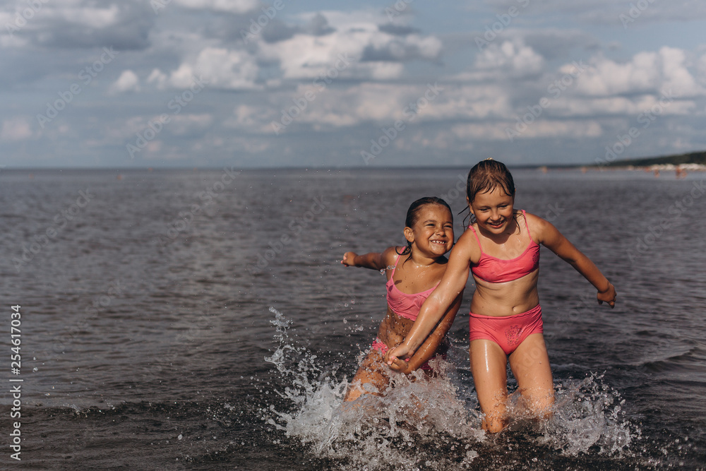Obraz premium Cheerful two girls playing on the ocean or sea beach having fun together, playing with water. Childhood, summer vacation, happines concept