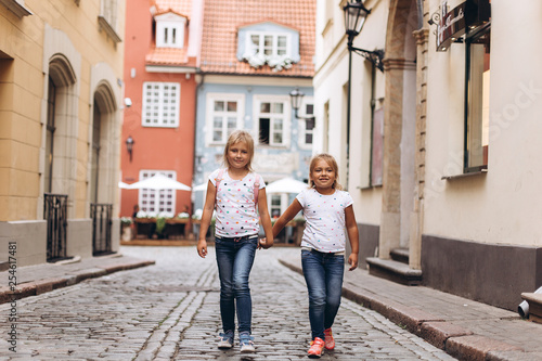 Cheerful happy girl travel together, hugging, holding hands and laughing outdoors in old town. Childhood, tourism, positive concept © Andreshkova Nastya