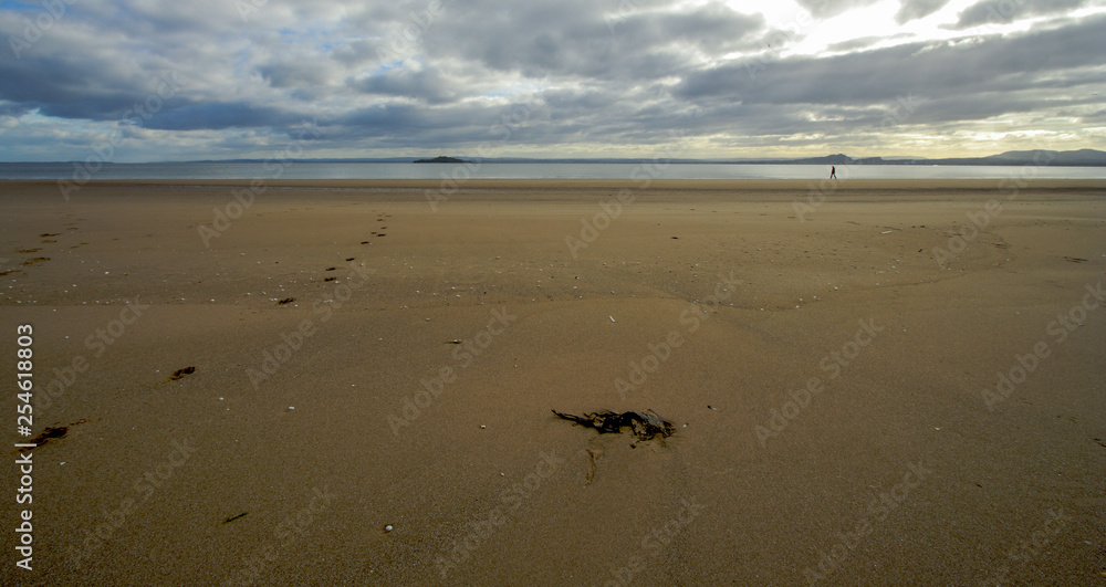 Fototapeta premium Wide sandy beach in winter at Kinghorn, Fife, Scotland with distant figure walking on shoreline