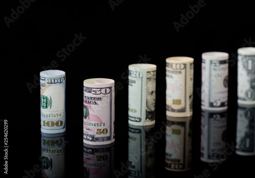 US dollars banknotes rolls on black background with reflection.