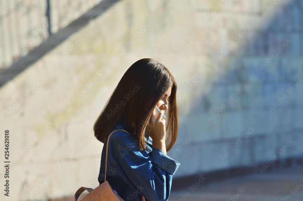 Fototapeta premium A young girl walks around the city with a pink backpack talking on the phone