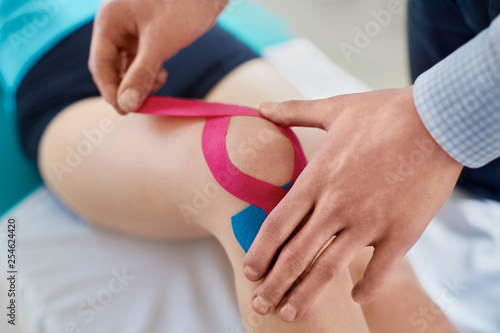 Kinesiology. Therapist taping knee with physio tape photo