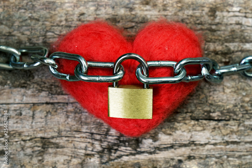 Red toy heart wrapped with a chain and closed with a metal lock. Love concept.