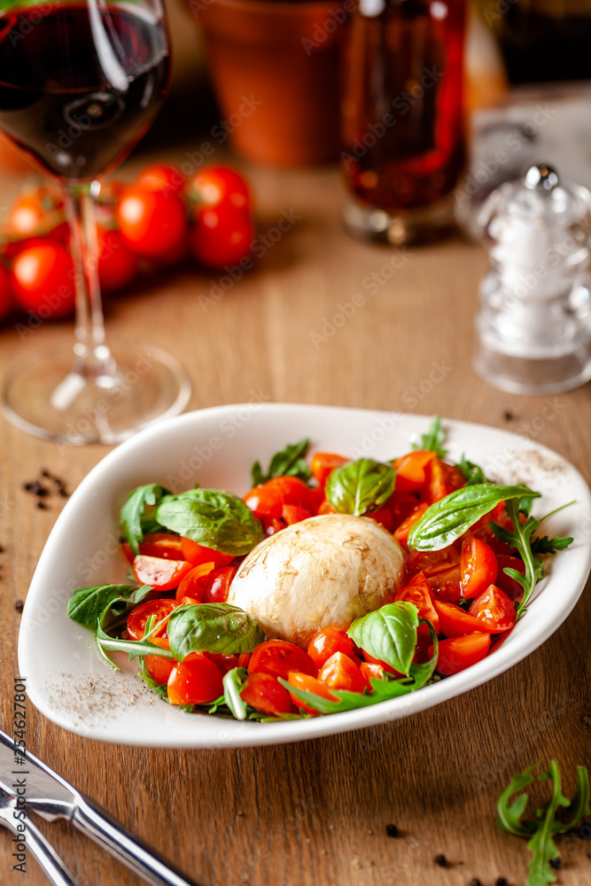 Concept of Italian cuisine. Caprese salad with cherry tomatoes, arugula and basil salad mix, and mozzarella cheese. Serving dishes in white plate in a restaurant. background image.