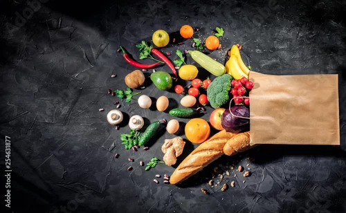Obraz Healthy food in full paper bag of different products vegetables and fruits on dark background