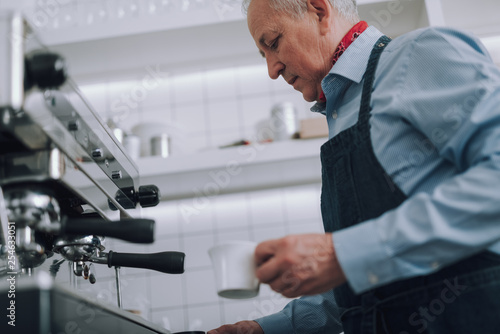 Elegant old man making hot drink with professional coffee machine