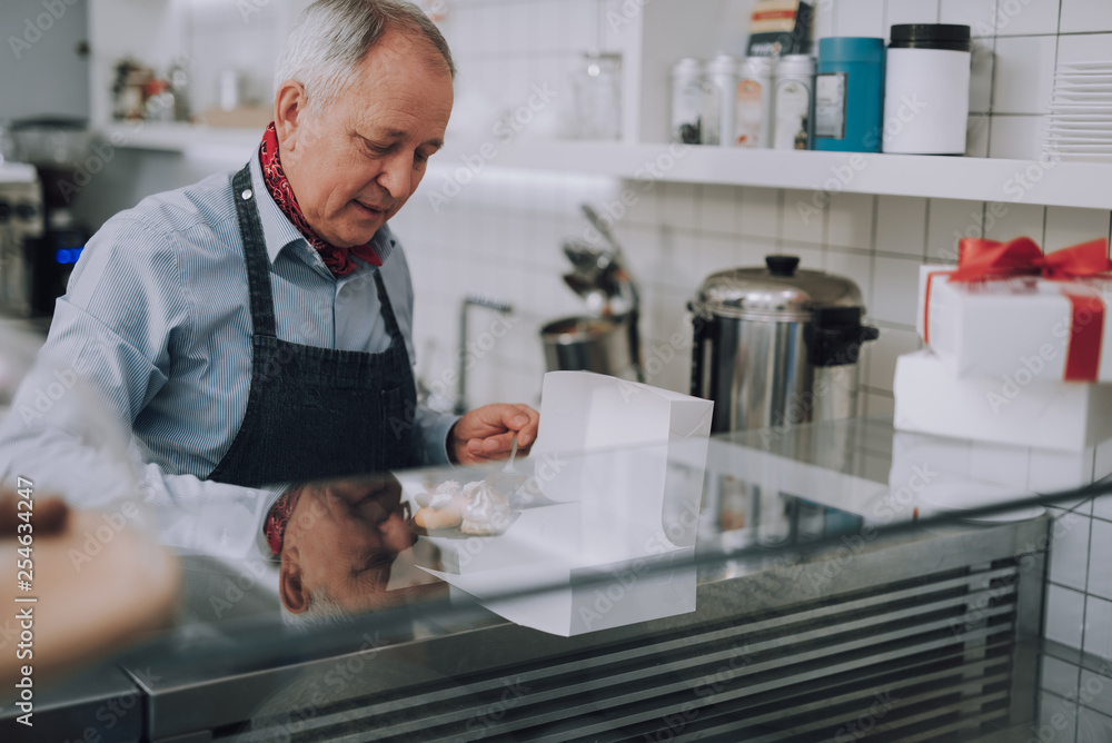 Senior man in apron preparing delicious pastries for special order Senior man in apron preparing delicious pastries for special order