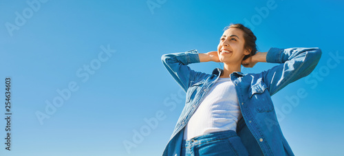 bottom view of a young smiling attractive woman in jeans clothes at sunny day on the blue sky background. joyful woman posing outdoors photo
