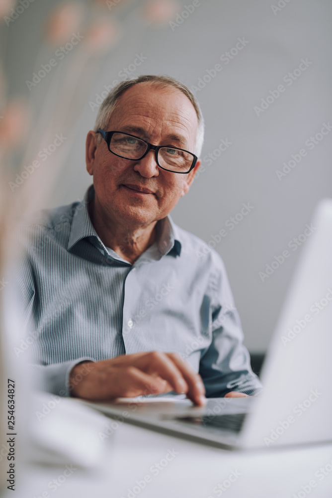 Good-looking old man in glasses using modern white laptop Good-looking old man in glasses using modern white laptop