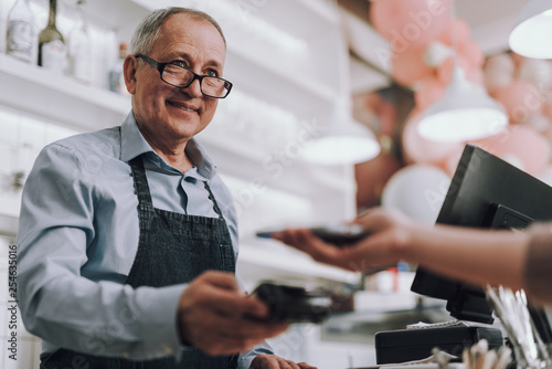 Friendly shop owner in glasses accepting payment from customer photo