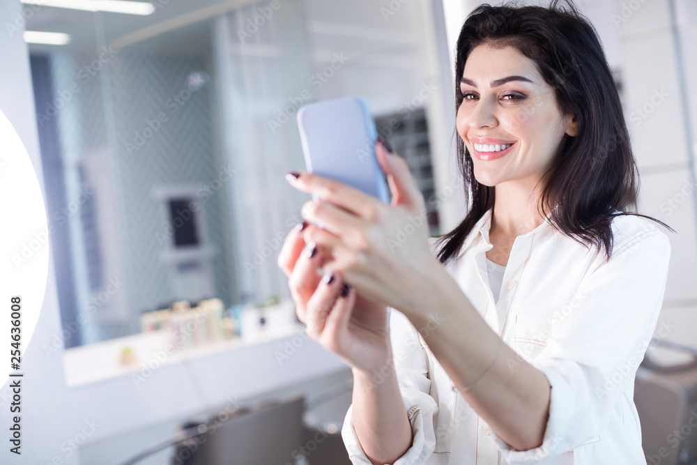 Low angle of smiling lady with cellphone in arms in hairdressing saloon Low angle of smiling lady with cellphone in arms in hairdressing saloon