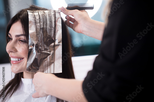 Smiling brunette woman dying her hair at the beauty salon