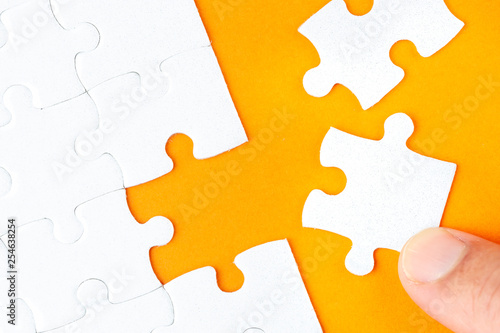 Hand holding piece of white puzzle on orange background