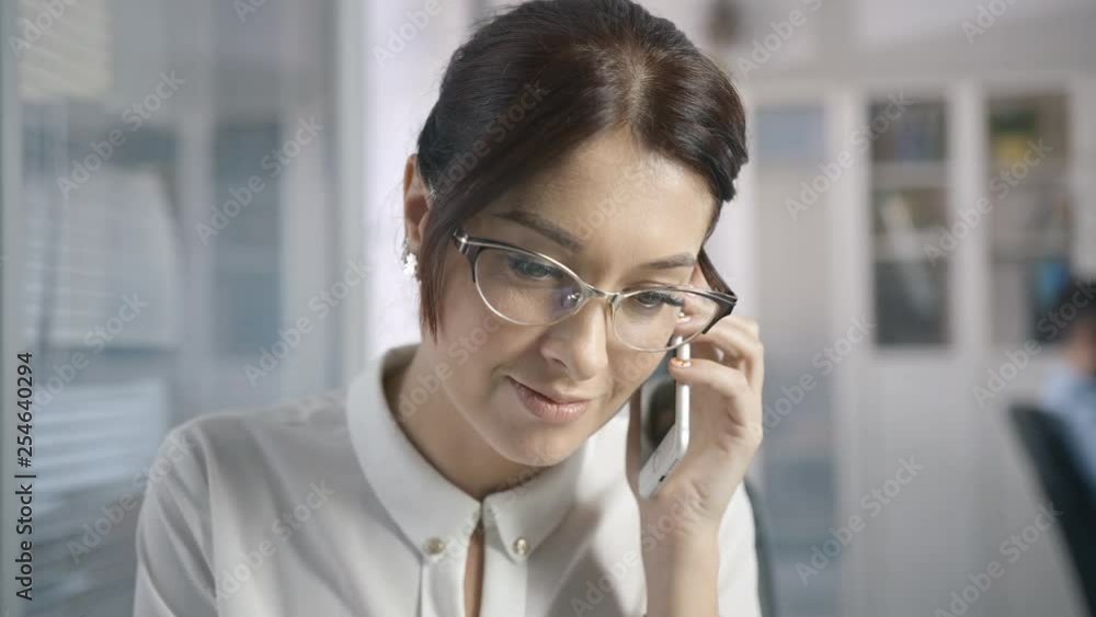Beautiful Female enjoy mobiles conversation. Smiling business White collar talking cellular. Person speaks phone in light room. Cheerful worker with documents and speaking mobile at office interior Beautiful Female enjoy mobiles conversation. Smiling business White collar talking cellular. Person speaks phone in light room. Cheerful worker with documents and speaking mobile at office interior