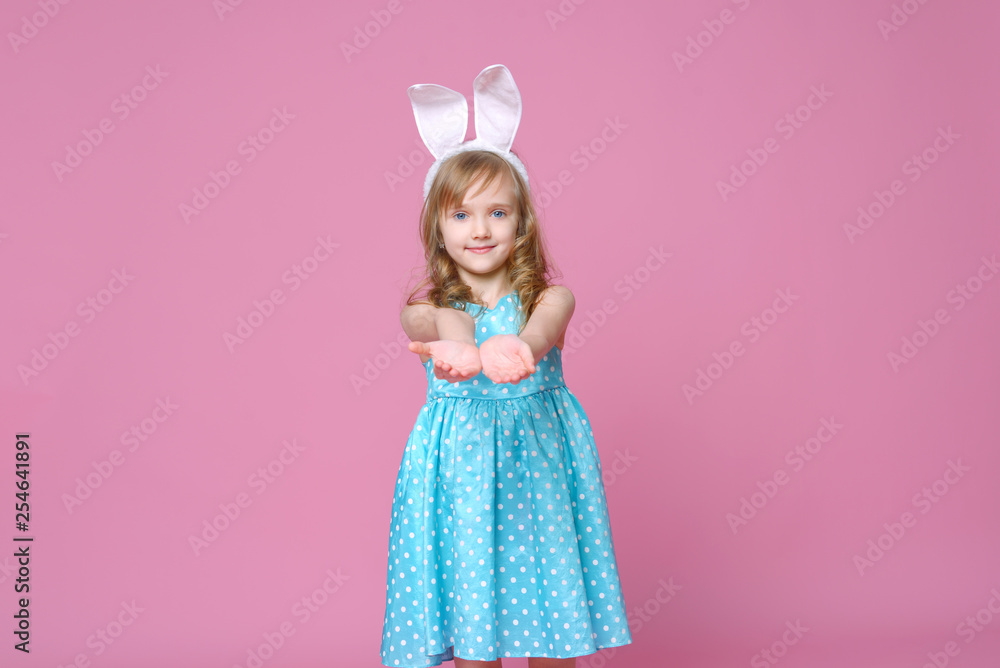 Cute little blonde girl in the shape of an Easter Bunny and a blue dress with a pea pattern. Concept of the celebration, advertising and fashion. happy Easter. Selective focus.