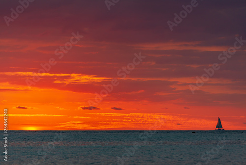 Sailing vessel sails on the burning sunset background on the calm surface of vastless Indian ocean
