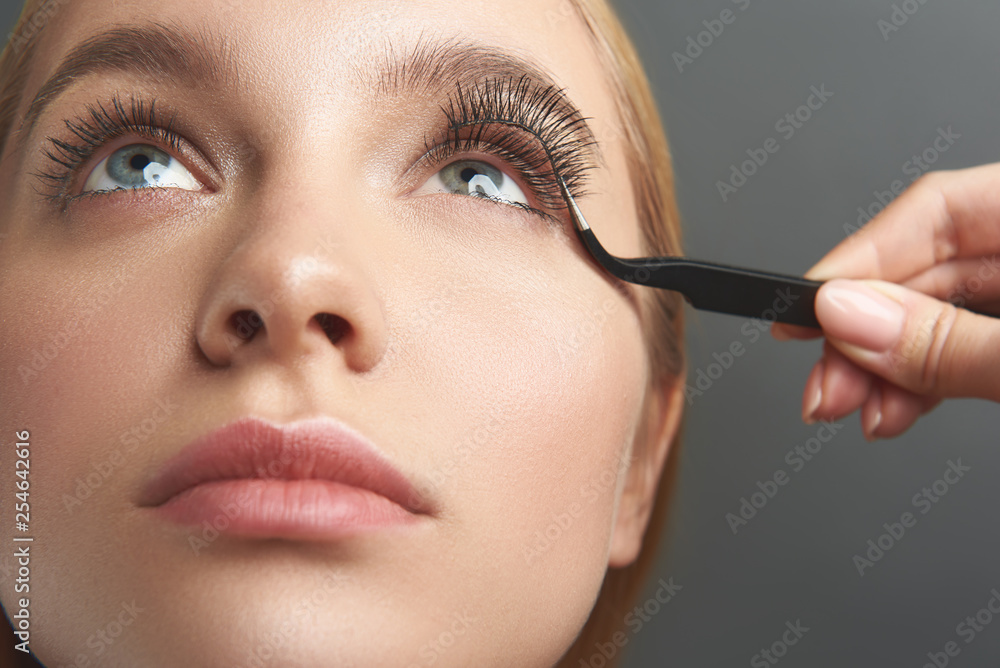Woman looking up while beautician applying false eyelashes
