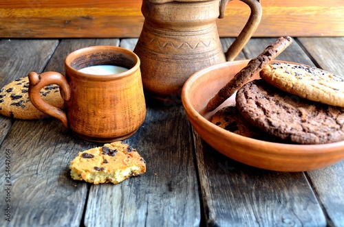 Oatmeal cookies in a ceramic rustic plate, milk in a ceramic mug, napkin, honey on a rustic wooden table.