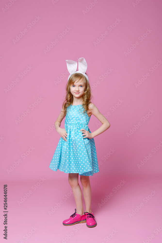 Cute little blonde girl in the shape of an Easter Bunny and a blue dress with a pea pattern. Concept of the celebration, advertising and fashion. happy Easter. Selective focus. Cute little blonde girl in the shape of an Easter Bunny and a blue dress with a pea pattern. Concept of the celebration, advertising and fashion. happy Easter. Selective focus.