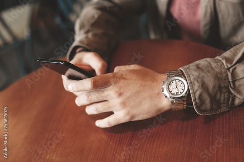 Young man with stylish wristwatch using modern cellphone