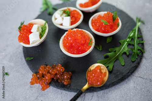 Red caviar on black plate with spoon and creamy cheese. Food photo concept