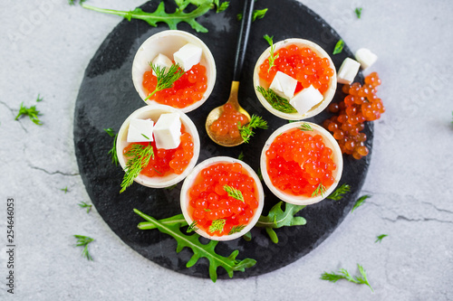 Red caviar on black plate with spoon and creamy cheese. Food photo concept