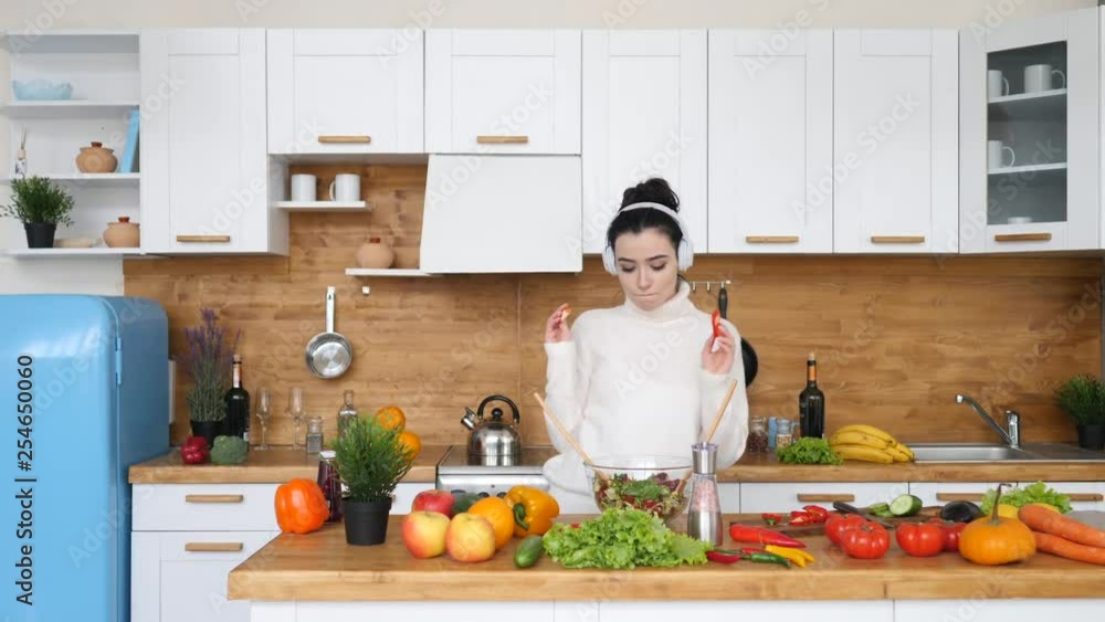 Young Brunette Woman Cooking In Kitchen Making Healthy Salad Dancing In Headphones. Young Brunette Woman Cooking In Kitchen Making Healthy Salad Dancing In Headphones.