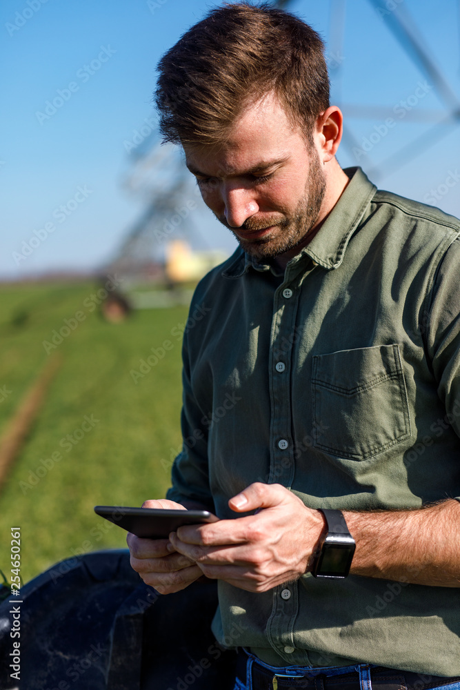Obraz premium Young farmer standing in wheat field and setup irrigation system on tablet.