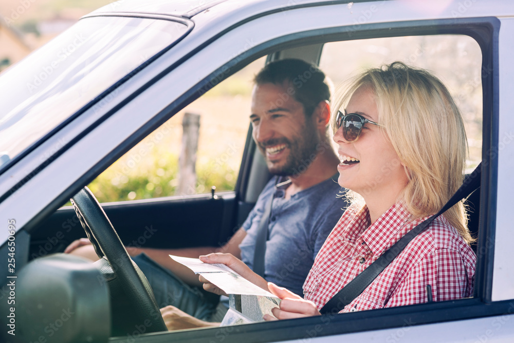 Happy couple traveling by car in nature and looking in map. Carefree friend travelers on countryside roadtrip journey. Happy couple traveling by car in nature and looking in map. Carefree friend travelers on countryside roadtrip journey.