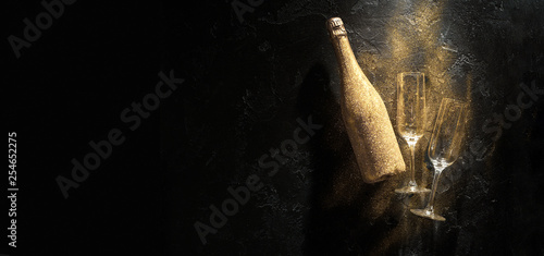 Photo of golden champagne bottle, two wine glasses on black stone background