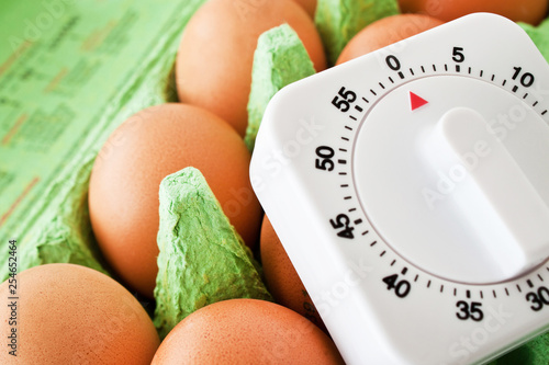 Egg timer and brown eggs in egg box photo