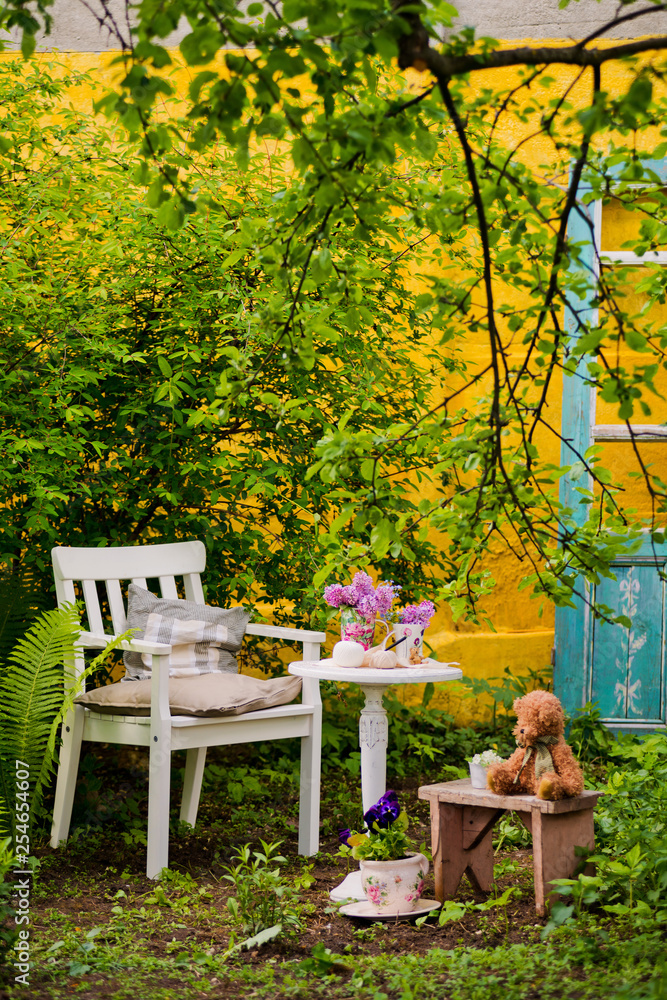 White wooden chair table with a bouquet of lilacs in the spring garden. Recreation area in the shade of trees own garden. Relax in nature. Clean air, peace for creativity and inspiration. fern, apple White wooden chair table with a bouquet of lilacs in the spring garden. Recreation area in the shade of trees own garden. Relax in nature. Clean air, peace for creativity and inspiration. fern, apple