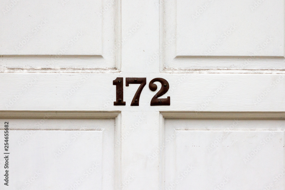 House number 172 with the one hundred and seventy two in bronze numerals in the middle of the wooden door cross and white panels House number 172 with the one hundred and seventy two in bronze numerals in the middle of the wooden door cross and white panels