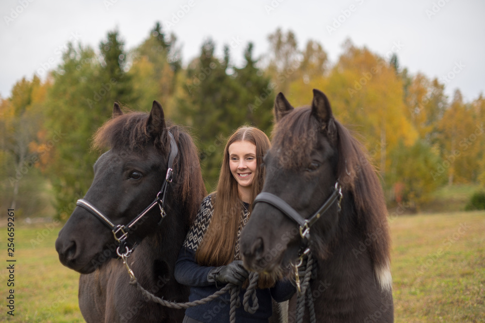 Obraz premium Smiling young swedish woman with her two black Icelandic horses