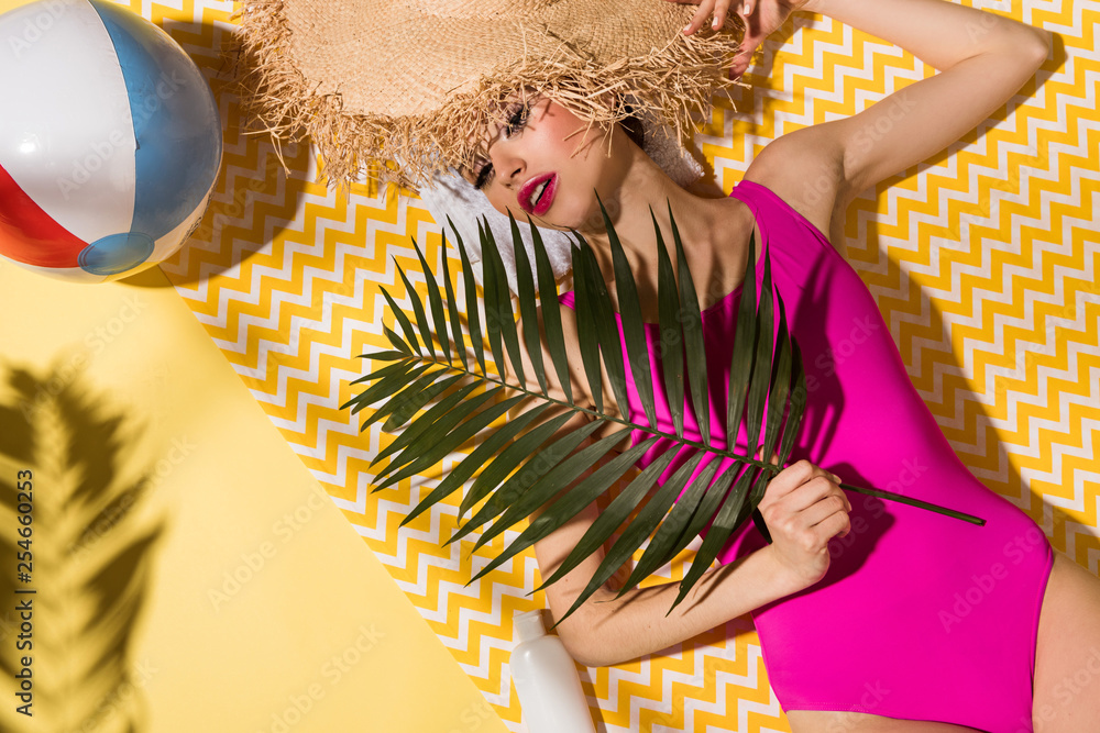 Φωτογραφία Top view of charming woman in pink swimsuit holding green plant and lying on yel