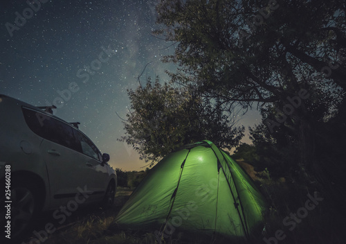 Camping with car and tent under the starry sky. Tourist car and green tent under bright night sky
