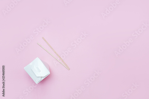 Opened takeaway box for chinese noodles presented with chopsticks, on pink background Retail set flatlay copyspace