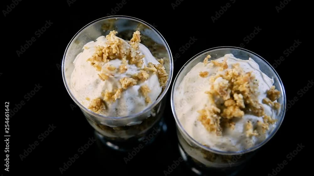 top view human hand put two white banana mousse dessert decorated with granola served in small round plastic glasses on black background top view human hand put two white banana mousse dessert decorated with granola served in small round plastic glasses on black background