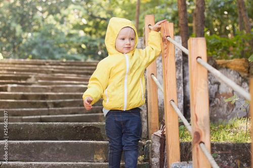 Funny two years girl in yellow raincoat walk in the park in sunny day