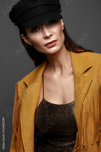 Beautiful girl with a classic make-up and a hairstyle in a fashionable designer jacket and cap, posing in the studio. Beauty face.