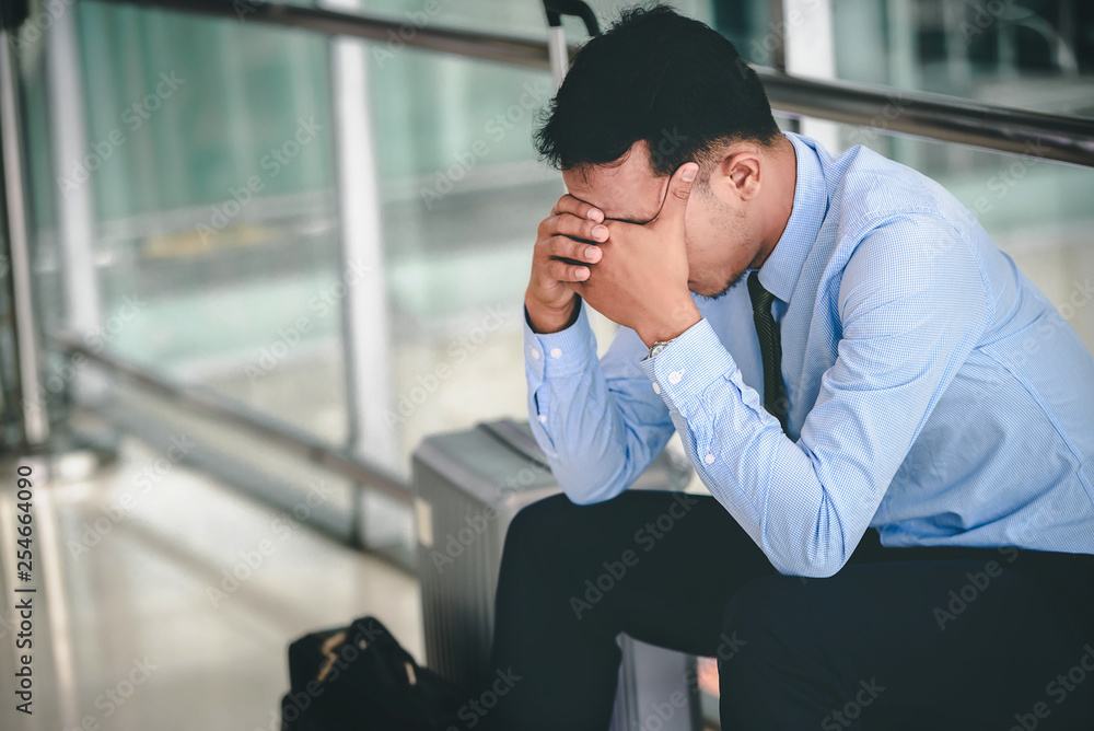 An Asian businessman is sitting on his luggage. He was stressed and looked at his smartphone at the airport. An Asian businessman is sitting on his luggage. He was stressed and looked at his smartphone at the airport.