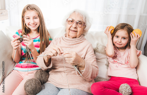 Smiling granddaughters with grandmother knitting together photo
