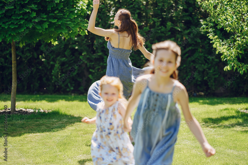 beautiful long-haired mother in a long blue dress in sunny summer forest walks with his beautiful daughters