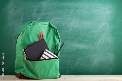 green backpack, black notebooks and pencils on the background of the blackboard