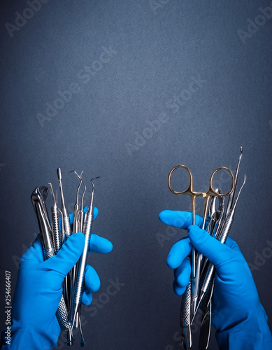 Hands in blue gloves holding metal dental equipment on gray background with copy space photo