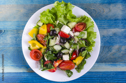 Vegetable salad cucumber capsicum tomato and olives on a white plate genuine blue background copy space